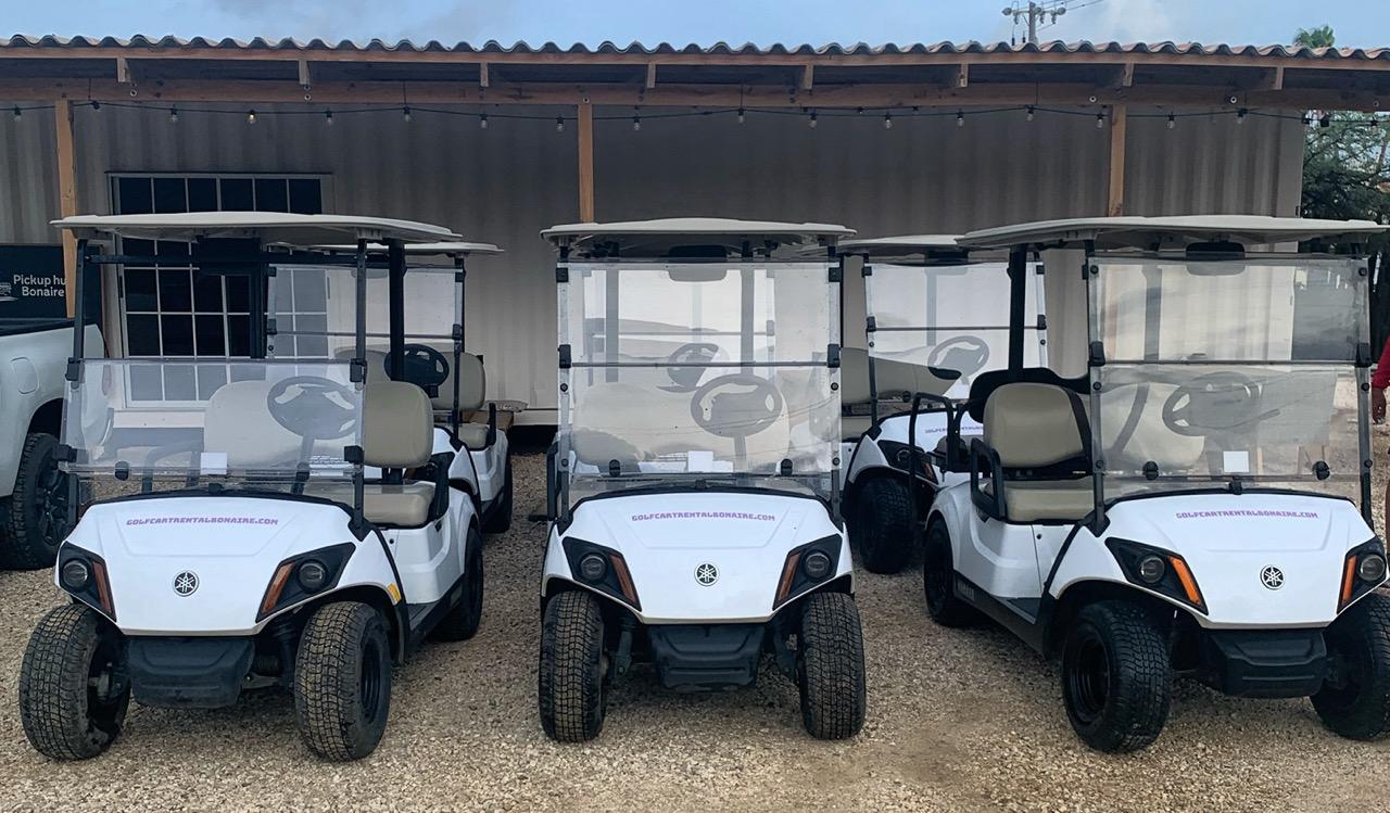 Belnem office of Golf Cart Rental Bonaire, with a lineup of ready-to-rent golf carts in front under a clear blue sky.